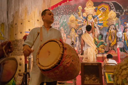 KOLKATA , INDIA - SEPTEMBER 27, 2017 : Young Hindu Priest worshipping Goddess Durga under holy smoke with dhaakis (drummers) performing. Durga Puja - shot at night under colored light .のeditorial素材