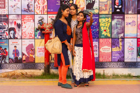 KOLKATA, INDIA - FEBRUARY 9TH , 2018 : Young Bengali Indian girls taking selfie in front of pictures of famous Indian writers and their books, at Kolkata book fair, world's largest book fair.のeditorial素材