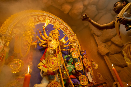 Kolkata, India - October 16, 2018 : Young Hindu Priest worshipping Goddess Durga with comch shell under holy smoke, Durga Puja festival ritual. - shot at night under colored light. Hindu Festival.のeditorial素材