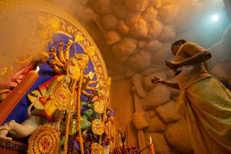 Kolkata, India - October 16, 2018 : Young Hindu Priest worshipping Goddess Durga with comch shell under holy smoke, Durga Puja festival ritual. - shot at night under colored light. Hindu Festival.のeditorial素材