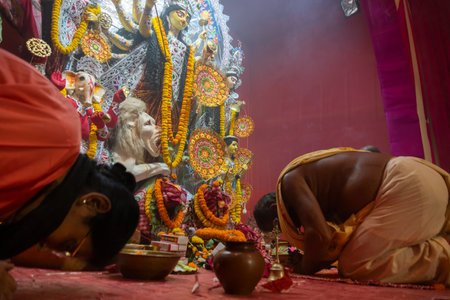 Kolkata, India - October 16, 2018 : Hindu Priest and Indian woman offering prayer to Goddess Durga, Durga Puja festival ritual- shot at colored light. Biggest festival of Hinduism celebrated worlwide.のeditorial素材