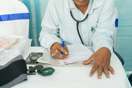 Kolkata, West Bengal, India - 25th February 2018 : Indian male Doctor writing prescription for a patient with medical instruments on his table.のeditorial素材