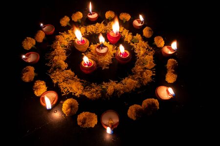 Side view of Rangoli flowers and candles or diyas placed beside them, Diwali lghts at night. Dark background Stock image.の写真素材