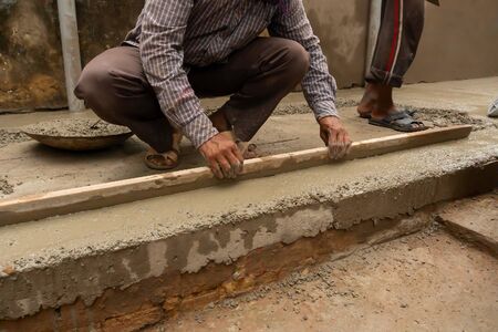 Indian construction worker levelling a cemented floor using wooden tool manually, Stock image.の写真素材