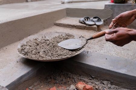 Indian labour preparing cement for plastering manually on bucket using trowel with bare hands. Stcok...