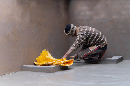 Howrah, West Bengal, India - 6th January 2020 : Indian labour levelling plastered floor using flat trowel and cement manually, In seated position. Stock image.のeditorial素材