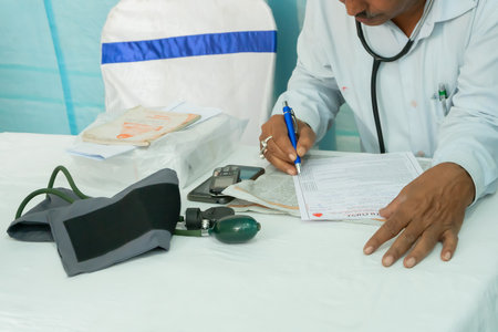 Kolkata, West Bengal, India - 25th February 2018 : Indian male Doctor writing prescription for a patient with medical instruments on his table.のeditorial素材