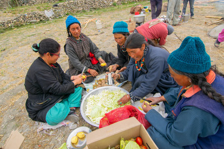 Mulbekh, Ladakh, India - 2nd September 2014 : Ladakhi tribal women in traditional dresses are cutting vegetables for preparing food for religious festival, Himalayan mountains in the background.のeditorial素材