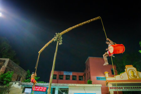 Howrah, West Bengal,India - 15th April 2019: Hindu devotee playing drum while hanging from pole in air, at night. Religious sports for festival called Charhak or Gajan, part of worshipping Lord Shiva.のeditorial素材