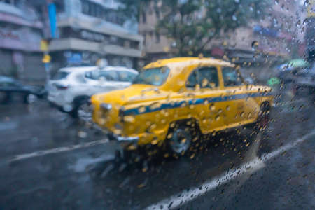 Raindrops falling on glass, abstract blurs - monsoon stock image of traditional yellow taxi of Kolkata (formerly Calcutta) city , West Bengal, Indiaの写真素材