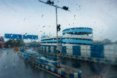 Raindrops falling on car windshield glass, abstract blurs of Nabanna building and road sign. Monsoon stock image of Howrah city , West Bengal, Indiaの写真素材
