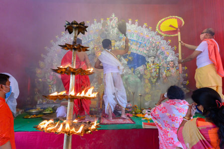 Howrah, West Bengal, India - 25th October 2020 : Goddess Durga is being worshipped by masked Hindu priest with holy panchapradip during sondhipujo aarti with holy smoke. Shonkho is played. Wide angle.のeditorial素材