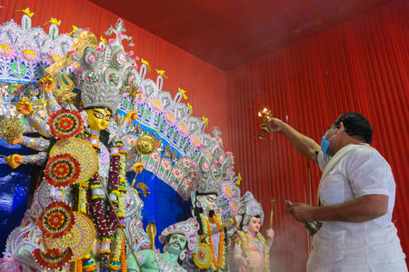 Howrah, West Bengal, India - 25th October 2020 : Goddess Durga is being worshipped by masked Hindu priest with holy panchapradip during sondhipujo aarti with holy smoke. Puja is Corona pandemic.のeditorial素材