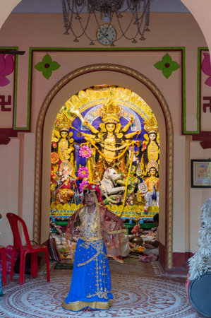 Howrah,India -October 26th,2020 : Bengali girl child posing with Goddess Durga in background, inside old age decorated home. Durga Puja, biggest festival of Hinduism, UNESCO heritage of humanity.のeditorial素材