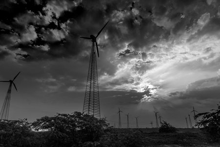 Silhouette of wind mills in twilight with a setting sun and cloudy sky in background, Rajasthan,...