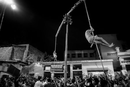 Howrah, West Bengal,India - 15th April 2019: Two Hindu devotees are hanging from pole in air, at night. Religious sports for festival called Charhak or Gajan. Black and white.のeditorial素材