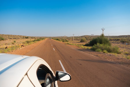White car running through empty high road or national high way passing through the desert. Distant horizon, Hot summer at Thar desert, Rajasthan, India.の写真素材