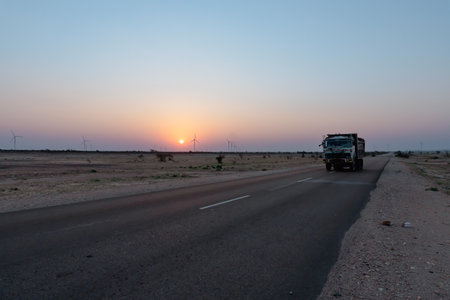 Dawn light in desert sky with empty road passing through the desert. Wind mills in the horizon, Sun rise at Thar desert, Rajasthan, India.の写真素材