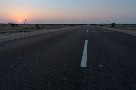 Dawn light in desert sky with empty road passing through the desert. Wind mills in the horizon, Sun rise at Thar desert, Rajasthan, India.の写真素材