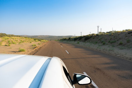 White car running through empty high road or national high way passing through the desert. Distant horizon, Hot summer at Thar desert, Rajasthan, India.の写真素材