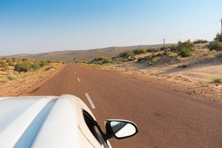 White car running through empty high road or national high way passing through the desert. Distant horizon, Hot summer at Thar desert, Rajasthan, India.の写真素材