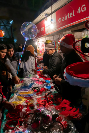 Kolkata, West Bengal, India - 25.12.2018 : Young people buying red hats and other festive gifts at roadside stall and enjoying themselves at illuminated and decorated park street with festive mood.のeditorial素材