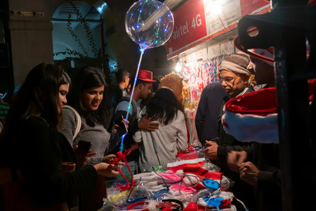 Kolkata, West Bengal, India - 25.12.2018 : Young people buying red hats and other festive gifts at roadside stall and enjoying themselves at illuminated and decorated park street with festive mood.のeditorial素材