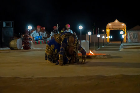 Thar desert, Rajasthan, India - October 15th 2019 : Rajasthani female dancer dancing, dressed with cultural dress, at night. Acrobatic dancer picking up currency note by mouth from dance floor.のeditorial素材