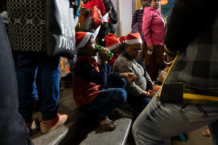 Kolkata, West Bengal, India - 26.12.2018 : Young boy enjoying drink with red santa claus hats enjoying themselves at illuminated and decorated park street with lights with year end festive mood.のeditorial素材