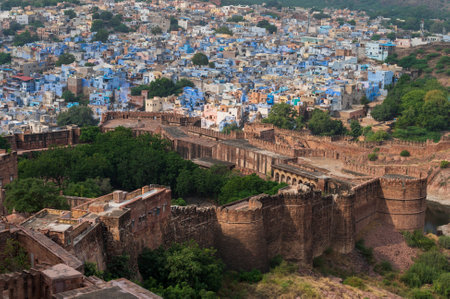 Top view of Mehrangarh fort with distant view of blue city Jodhpur, Rajasthan, India. Blue sky with white clouds in the background. One of the seven gates to enter the huge fort is seen below,の写真素材