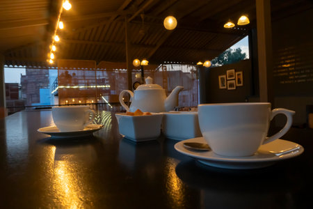 Beautiful interior view of restaurant at Jodhpur, Rajasthan, India. White cups, dishes and tea pot with reflection of decorated lights on shining table top.の写真素材