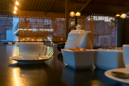 Beautiful interior view of restaurant at Jodhpur, Rajasthan, India. White cups, dishes and tea pot with reflection of decorated lights on shining table top.の写真素材