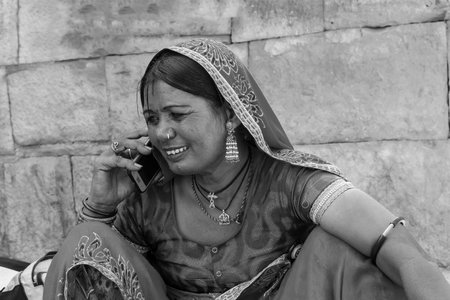 Jaisalmer, Rajasthan, India - October 13, 2019 : Rajasthani woman smiling while talking in mobile phone in market place Inside Jaisalmer Fort. Happy woman of Jaisalmer.のeditorial素材
