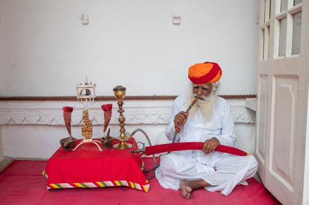 Jodhpur,Rajasthan,India - 19th October 2019: Rajput senior man smoking through a hookah, wearing Marathi pagri and sword on knees. Hookah is instrument for vapourizing and smoking flavoured tobacco.のeditorial素材