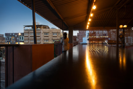 Indian solo traveller woman photographer taking picture outside. Beautiful interior view of restaurant at Jodhpur, Rajasthan, India. Reflection of decorated lights on shining table top.の写真素材