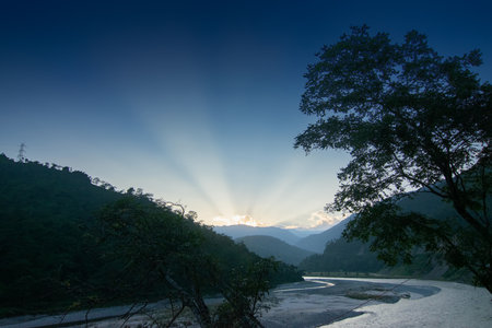 Teesta river flowing through Himalayan mountains, sunlight coming through clouds in the background,...