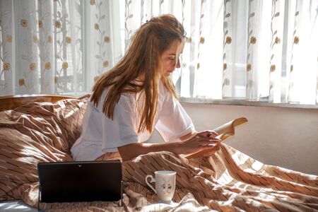 young woman in the bed welcome to first sunlight of the morning by working at homeの写真素材