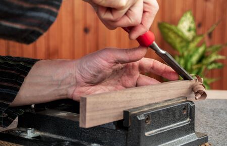 a closeup opposite angle scene of hands of a male carpenter, planing wooden plank with chisel - wood plank is locked in the iron viseの写真素材