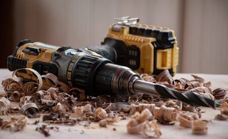 an old very used hand drill power tool lies on the workbench with wood chipsの写真素材