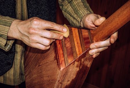 polishing wooden musical instrument with sponge, oriental stringed instrument lavta being polished with shellac, closeup.の写真素材