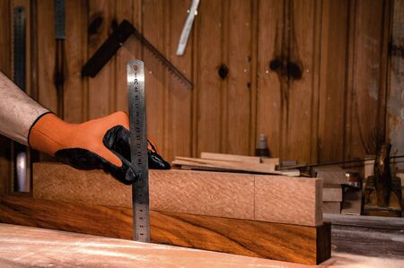 worker measuring work pieces with metal ruler, hands only with protective glove, on the workbench in carpentry workshop, closeup.の写真素材