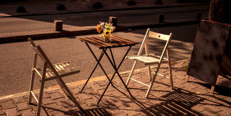 wooden foldable table and chairs on the street, as an outdoor coffee shop. cafe table with flower under the warm sun light.の写真素材