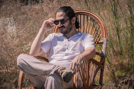 a young man in black sunglasses sits in a wicker chair charismatically, outdoors and in a sunny summer day.の写真素材