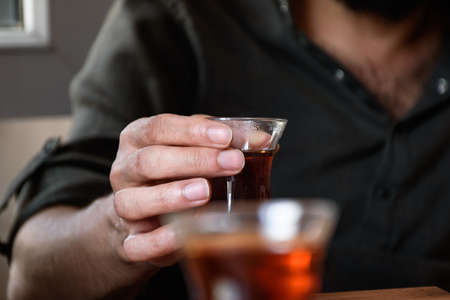 a man holding a cup of turkish tea, hands only, second tea glass in blur foreground.の写真素材