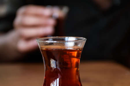 closeup view of a glass of turkish tea and a man holding another one in blur background. drinking tea together.の写真素材