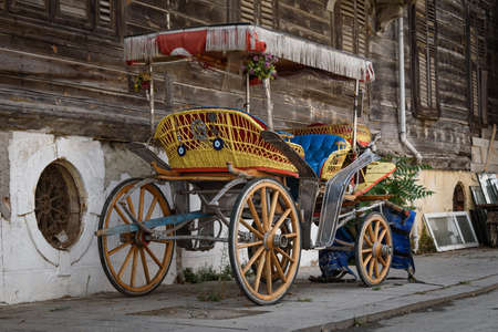 A colorful horse-drawn carriage parked in front of an old wooden house.
