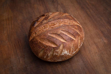 thick crust organic round village bread on the brown wooden platform, close-up.の写真素材