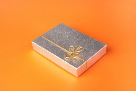 A silver gift package with a golden ribbon on a orange backgroundの写真素材