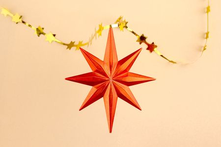 Christmas decoration orange star on sand background with gold garland. Would be perfect for a...