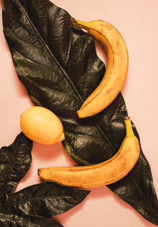 Bananas and lemon lying on the leaves and pink backgroundの写真素材